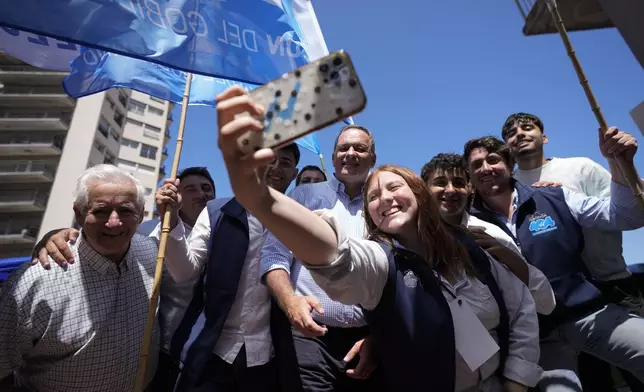 Alvaro Delgado, presidential candidate for the ruling National Party, center, poses for a selfie with supporters outside a polling station during general elections in Montevideo, Uruguay, Sunday, Oct. 27, 2024. (AP Photo/Natacha Pisarenko)