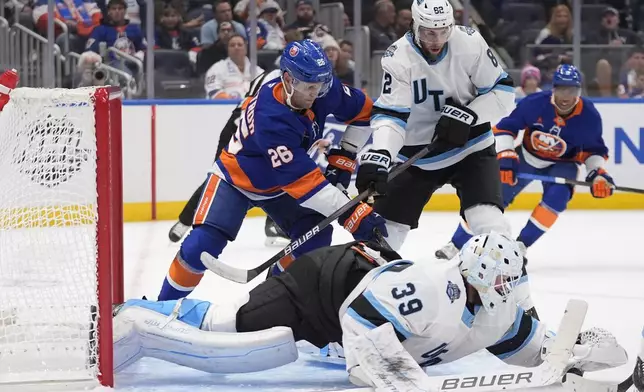 Utah Hockey Club goaltender Connor Ingram (39) reaches for the puck as Karel Vejmelka (82) defends New York Islanders' Oliver Wahlstrom (26) during the second period of an NHL hockey game Thursday, Oct. 10, 2024, in Elmont, N.Y. (AP Photo/Frank Franklin II)