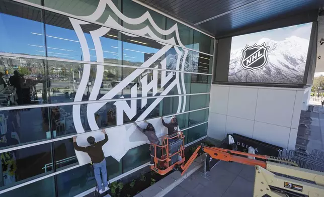 FILE - Workers put up signs celebrating the sale of the Arizona Coyotes and its accompanying relocation to Salt Lake City, at the Delta Center on Thursday, April 18, 2024, in Salt Lake City. (AP Photo/Rick Bowmer, File)