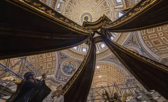 Journalists snap photos, Tuesday, Oct. 8, 2024, to the almost completed restoration works of Bernini's monumental bronze canopy, situated beneath Michelangelo's massive dome after the gleaming bronze of its twisting Solomonic columns has been concealed by scaffolds for nine months while expert conservators worked meticulously on its intricate surface. (AP Photo/Domenico Stinellis)