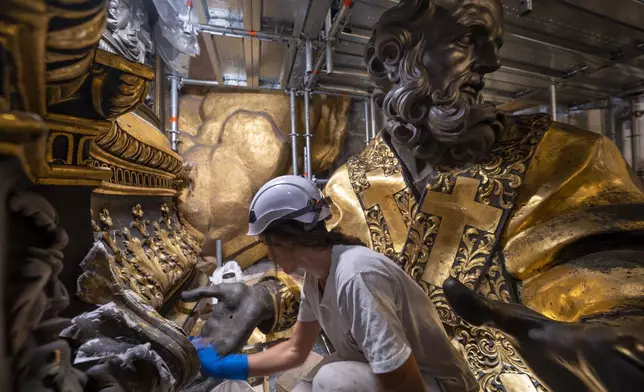 Restorer Eleonora Di Vittorio works, Tuesday, Oct. 8, 2024, in front of a bronze statue of St John Chrysostom, right, part of the Cathedra of St. Peter's inside St. Peter's Basilica at The Vatican where Bernini's monumental bronze canopy has been under restoration too since February by expert conservators who worked meticulously on its intricate surface. (AP Photo/Domenico Stinellis)