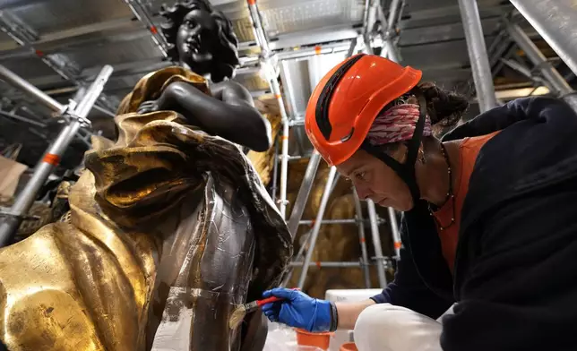 Restorer Romana Albini attends, Tuesday, Oct. 8, 2024, to the restoration of a bronze statue of an angel, left, part of the Cathedra of St. Peter's inside St. Peter's Basilica at The Vatican where Bernini's monumental bronze canopy has been under restoration too since February by expert conservators who worked meticulously on its intricate surface. (AP Photo/Domenico Stinellis)