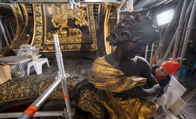 Restorer Romana Albini attends, Tuesday, Oct. 8, 2024, to the restoration of a bronze statue of an angel, left, part of the Cathedra of St. Peter's inside St. Peter's Basilica at The Vatican where Bernini's monumental bronze canopy has been under restoration too since February by expert conservators who worked meticulously on its intricate surface. (AP Photo/Domenico Stinellis)