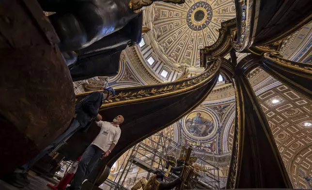 Restorer Sante Guido, right, shows to journalists, Tuesday, Oct. 8, 2024, the end of the restoration works of Bernini's monumental bronze canopy, situated beneath Michelangelo's massive dome after the gleaming bronze of its twisting Solomonic columns has been concealed by scaffolds for nine months while expert conservators worked meticulously on its intricate surface. (AP Photo/Domenico Stinellis)