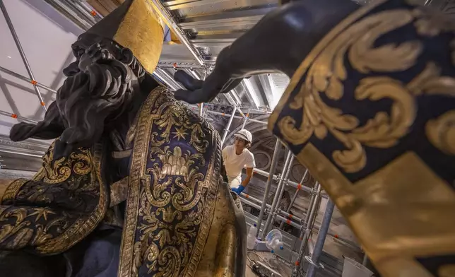 Restorer Elisabetta De Narda attends, Tuesday, Oct. 8, 2024, at the restoration of an almost six-meter tall bronze statue of Saint Ambrose, left, part of the Cathedra of St. Peter's inside St. Peter's Basilica at The Vatican where Bernini's monumental bronze canopy has been under restoration too since February by expert conservators who worked meticulously on its intricate surface. (AP Photo/Domenico Stinellis)