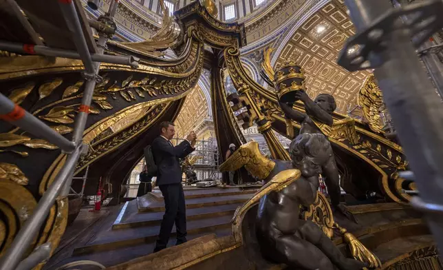 Experts show to journalists, Tuesday, Oct. 8, 2024, the restoration works of Bernini's monumental bronze canopy, situated beneath Michelangelo's massive dome and towering 95 feet above the papal altar that sits directly above the Tomb of Saint Peter inside St. Peter's Basilica at The Vatican, where the gleaming bronze of its twisting Solomonic columns has been concealed by scaffolds for nine months while expert conservators worked meticulously on its intricate surface. (AP Photo/Domenico Stinellis)