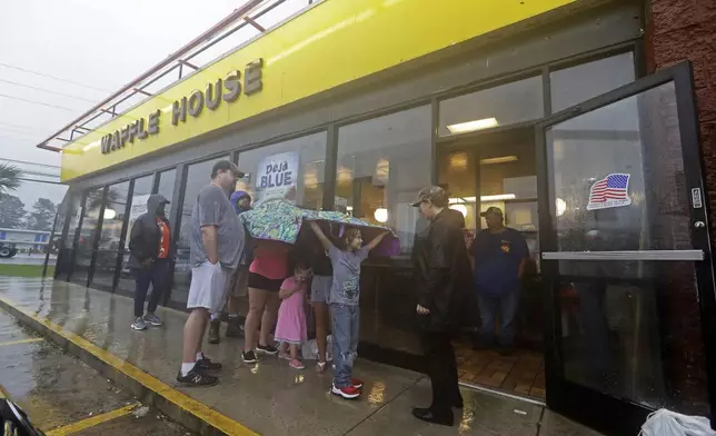 FILE - Luke Churchill, left, stands with his wife, Mary and their children, Katie, 13, Liam, 9, and Raighan, 3, as they wait in the rain outside an open Waffle House restaurant in Wilmington, N.C., after Hurricane Florence traveled through the area, Sept. 16, 2018. (AP Photo/Chuck Burton, File)