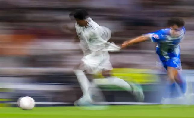 In this image taken with a slow shutter speed, Real Madrid's Rodrygo, left, duels for the ball with Alaves' Carlos Benavidez during a Spanish La Liga soccer match between Real Madrid and Alaves at Santiago Bernabeu stadium in Madrid, Spain, Tuesday, Sept. 24, 2024. (AP Photo/Manu Fernandez)