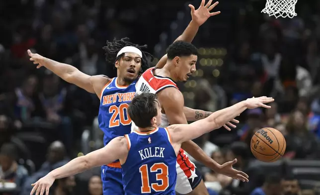 Washington Wizards guard Johnny Davis, top right, passes the ball off under the basket against New York Knicks center Jericho Sims (20) and Tyler Kolek (13) during the second half of an NBA preseason basketball game Friday, Oct. 18, 2024, in Washington. (AP Photo/John McDonnell)