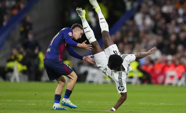 Real Madrid's Aurelien Tchouameni, right, falls next to Barcelona's Marc Casado during a Spanish La Liga soccer match between Real Madrid and Barcelona at the Santiago Bernabeu stadium in Madrid, Spain, Saturday, Oct. 26, 2024. (AP Photo/Manu Fernandez)