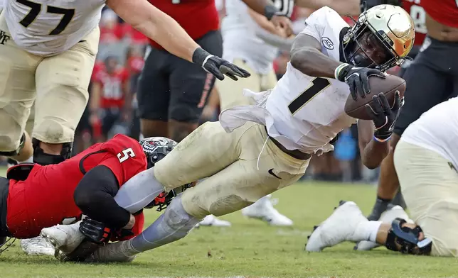 Wake Forest running back Demond Claiborne (1) stretches in the grasp of North Carolina State's DK Kaufman (5) during the second half of an NCAA college football game in Raleigh, N.C., Saturday, Oct. 5, 2024. (AP Photo/Karl B DeBlaker)