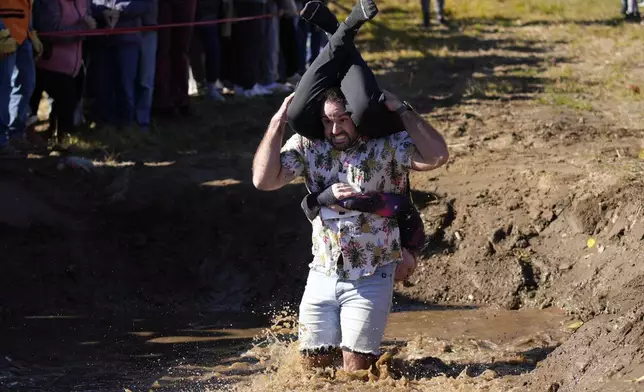 Michael Batakis carries Hannah Batakis through a muddy water pit during the North American Wife Carrying Championship, Saturday, Oct. 12, 2024, at Sunday River ski resort in Newry, Maine. (AP Photo/Robert F. Bukaty)