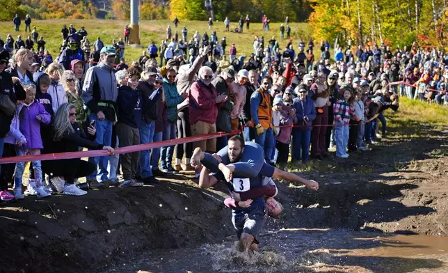 Jon Heaner splashes through the water hazard while carrying Renee Heaner during the North American Wife Carrying Championship, Saturday, Oct. 12, 2024, at Sunday River ski resort in Newry, Maine. (AP Photo/Robert F. Bukaty)