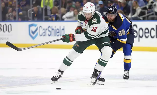 Minnesota Wild's Matt Boldy (12) and St. Louis Blues' Pavel Buchnevich (89) vie for control of the puck during the first period of an NHL hockey game Tuesday, Oct. 15, 2024, in St. Louis. (AP Photo/Scott Kane)