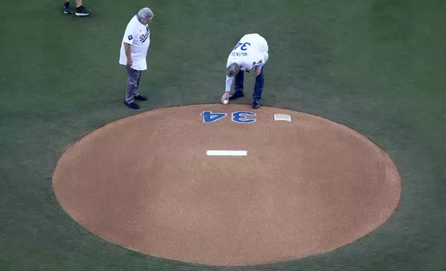 Former Los Angeles Dodgers players Steve Yeager, left, and Orel Hershiser place a ball on the mound in honor of Fernando Valenzuela before Game 1 of the baseball World Series, Friday, Oct. 25, 2024, in Los Angeles. (AP Photo/Mark J. Terrill)