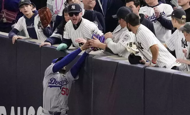 Fans interfere with a foul ball caught by Los Angeles Dodgers right fielder Mookie Betts during the first inning in Game 4 of the baseball World Series against the New York Yankees, Tuesday, Oct. 29, 2024, in New York. (AP Photo/Ashley Landis)