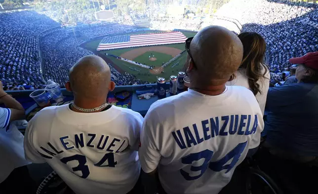 Fans stand during the national antehm before Game 1 of the baseball World Series, Friday, Oct. 25, 2024, in Los Angeles. (AP Photo/Julio Cortez)