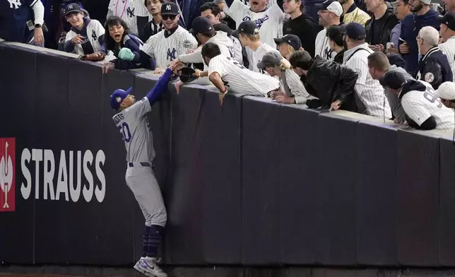 Fans interfere with a foul ball caught by Los Angeles Dodgers right fielder Mookie Betts during the first inning in Game 4 of the baseball World Series against the New York Yankees, Tuesday, Oct. 29, 2024, in New York. (AP Photo/Ashley Landis)