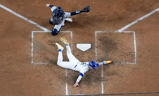 Los Angeles Dodgers' Kiké Hernández, bottom, scores past New York Yankees catcher Austin Wells on a sacrifice fly ball by Will Smith during the fifth inning in Game 1 of the baseball World Series, Friday, Oct. 25, 2024, in Los Angeles. (AP Photo/Mark J. Terrill)