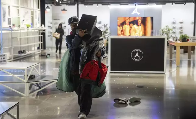 People carries out items from a ransacked Nike store after the Los Angeles Dodgers defeated the New York Yankees to win the baseball World Series Wednesday, Oct. 30, 2024, in Los Angeles. (AP Photo/Ethan Swope)