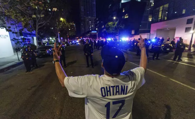 A fan wearing a Shohei Ohtani taunts Los Angeles Police officers as fans celebrate on the streets after the Los Angeles Dodgers won against the New York Yankees in the baseball World Series Wednesday, Oct. 30, 2024, in downtown Los Angeles. (AP Photo/Damian Dovarganes)