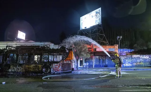 Firefighters douse water on a bus that was set on fire at Sunset and Echo Park after people gathered on the streets after the Los Angeles Dodgers defeated the New York Yankees to win the baseball World Series early Thursday, Oct. 31, 2024, in Los Angeles. (AP Photo/Ethan Swope)