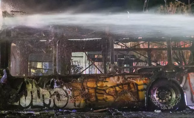 Firefighters douse water on a bus that was set on fire at Sunset and Echo Park after people gathered on the streets after the Los Angeles Dodgers defeated the New York Yankees to win the baseball World Series early Thursday, Oct. 31, 2024, in Los Angeles. (AP Photo/Ethan Swope)