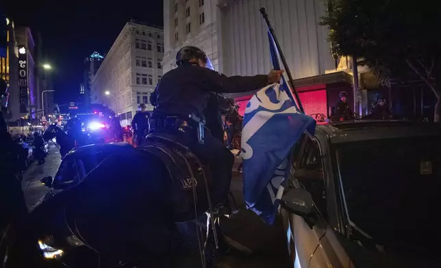 A police officer on horseback grabs a Los Angeles Dodgers flag as people gather on the streets after the Los Angeles Dodgers won against the New York Yankees in the baseball World Series Wednesday, Oct. 30, 2024, in Los Angeles. (AP Photo/Ethan Swope)