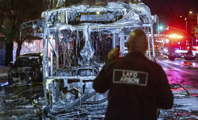 An LAFD arson investigator inspects a bus that was set on fire at Sunset and Echo Park after people gathered on the streets after the Los Angeles Dodgers defeated the New York Yankees to win the baseball World Series early Thursday, Oct. 31, 2024, in Los Angeles. (AP Photo/Ethan Swope)