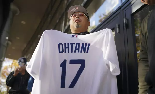 A man shows off a baseball jersey of Shohei Ohtani of the Los Angeles Dodgers as he and others wait in line to watch a live stream of Game 3 of the baseball World Series between the Dodgers and the New York Yankees, in a public viewing event in Oshu, northeastern Japan, the hometown of Ohtani, Tuesday, Oct. 29, 2024. (AP Photo/Eugene Hoshiko)