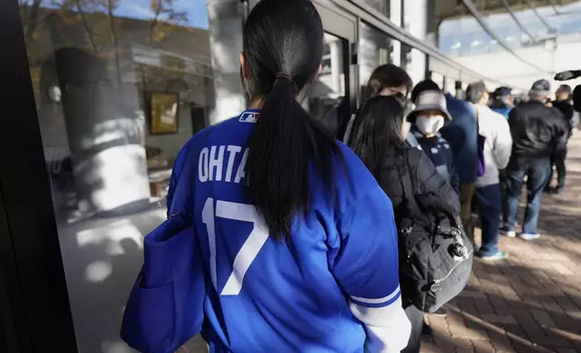 A woman wearing a baseball jersey of Shohei Ohtani of the Los Angeles Dodgers and others wait in line to watch a live stream of Game 3 of the baseball World Series between the Los Angeles Dodgers and the New York Yankees, in a public viewing event in Oshu, northeastern Japan, the hometown of Ohtani, Tuesday,Oct. 29, 2024. (AP Photo/Eugene Hoshiko)