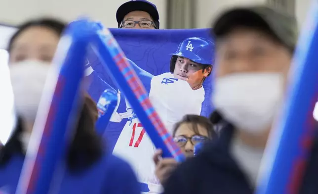 A man brings up a poster of Shohei Ohtani of the Los Angeles Dodgers as he and others watch a live view of Game 4 of the baseball World Series between the Dodgers and the New York Yankees during a public viewing event in Oshu, northeastern Japan, the hometown of Ohtani, Wednesday, Oct. 30, 2024. (AP Photo/Eugene Hoshiko)