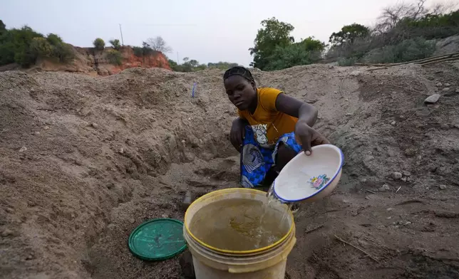 A woman scoops water from a hole she has dug in a dried up riverbed in Lusitu, Zambia, Wednesday, Sept. 18, 2024. (AP Photo/Themba Hadebe)