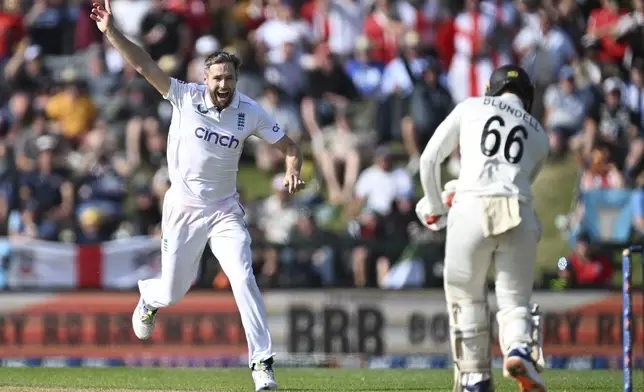 England bowler Chris Woakes runs down the wicket as he celebrates the dismissal of New Zealand batsman Tom Blundell, right, during play on the third day of the first cricket test between England and New Zealand at Hagley Oval in Christchurch, New Zealand, Saturday, Nov. 30, 2024. (Andrew Cornaga/Photosport via AP)