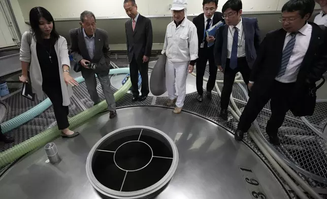 An interpreter, left, translates for Junichiro Ozawa, head of Ozawa Sake Brewery, third left, and his worker (in white) as Hitoshi Utsunomiya, far right, director of the Japan Sake and Shochu Makers Association, stands during a media tour at the brewery in Ome, on the western outskirts of Tokyo, Japan, Wednesday, Nov. 13, 2024. (AP Photo/Hiro Komae)