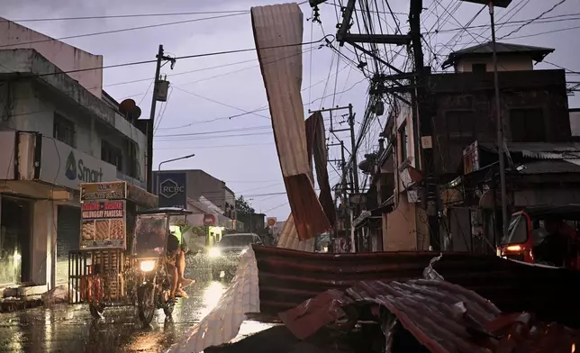 Motorists ride past a part of a roof suspended on electric wires blown by strong winds caused by Typhoon Man-yi along a street in the municipality of Baler, Aurora province, Philippines, Monday, Nov. 18, 2024. (AP Photo/Noel Celis)