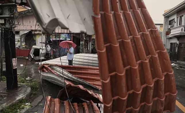 A man walks past roof sheets suspended on electric wires blown by strong winds caused by Typhoon Man-yi along a street in the municipality of Baler, Aurora province, northeastern Philippines, Monday, Nov. 18, 2024. (AP Photo/Noel Celis)