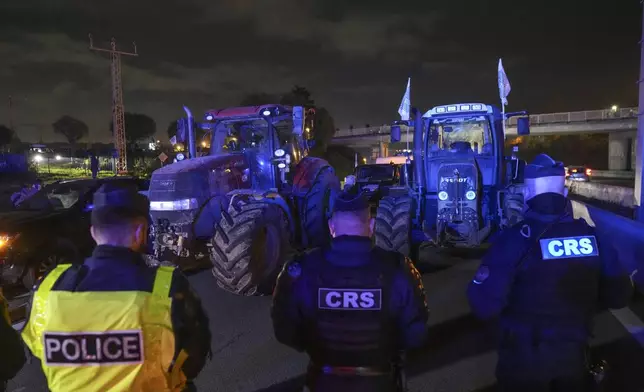 Police officers stand in front of tractors on a blocked highway in Velizy-Villacoublay, outside Paris, Sunday, Nov. 17, 2024. (AP Photo/Michel Euler)