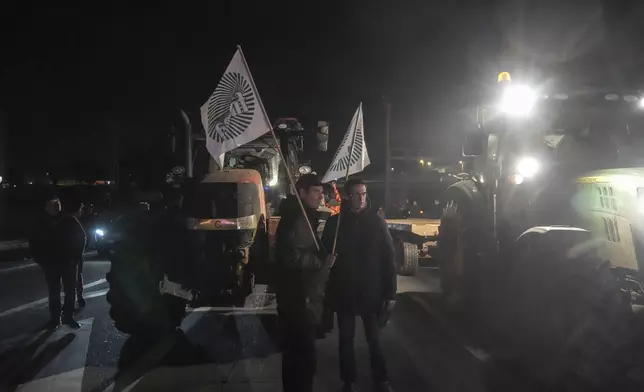 Farmers hold union flags as they stand between tractors on a blocked highway in Velizy-Villacoublay, outside Paris, Sunday, Nov. 17, 2024. (AP Photo/Michel Euler)