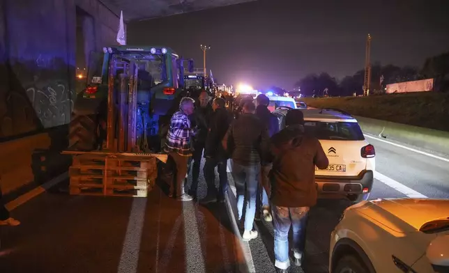 Farmers walk between tractors and cars on a blocked highway in Velizy-Villacoublay, outside Paris, Sunday, Nov. 17, 2024. (AP Photo/Michel Euler)