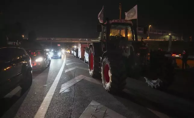 Cars drive along tractors on a blocked highway in Velizy-Villacoublay, outside Paris, Sunday, Nov. 17, 2024. (AP Photo/Michel Euler)