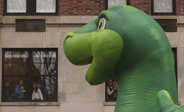 Spectators watch from an apartment window as the Sinclair's Dino balloon passes by during the Macy's Thanksgiving Day Parade, Thursday, Nov. 28, 2024, in New York. (AP Photo/Yuki Iwamura)