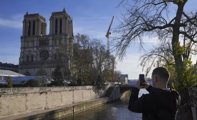 A man takes a picture of Notre Dame Cathedral as French President Emmanuel Macron visits the renovated cathedral, Friday, Nov. 29, 2024 in Paris. (AP Photo/Michel Euler)