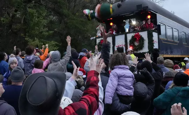 People reach for toys tossed from the CSX Santa Train, Saturday, Nov. 23, 2024, in Elkhorn City, Ky. The train brings presents to small towns along a 110-mile portion of the railroad line in rural Appalachian Tennessee, Kentucky and Virginia. (AP Photo/George Walker IV)