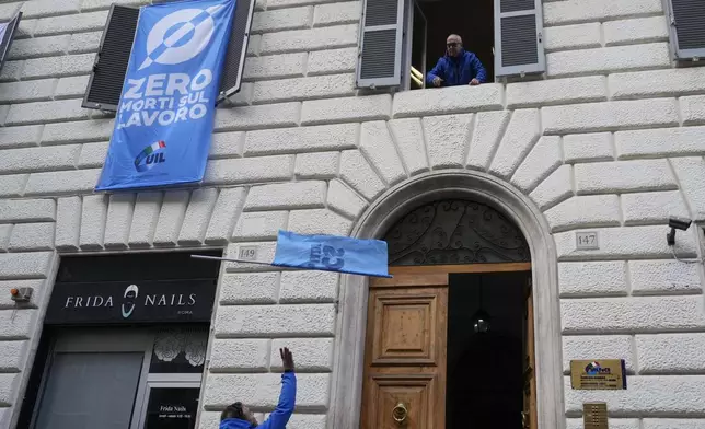 A demonstrator grabs a flag thrown from a labor unions headquarters showing a banner at left reading: "zero deaths at work" during a public and private sectors' national strike to protest against government's budget law in Rome, Friday, Nov. 29, 2024. (AP Photo/Gregorio Borgia)