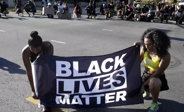 FILE - Alycia Pascual-Pena, left, and Marley Ralph kneel while holding a Black Lives Matter banner during a protest in memory of Breonna Taylor, in Los Angeles, July 11, 2020. (AP Photo/Marcio Jose Sanchez, File)