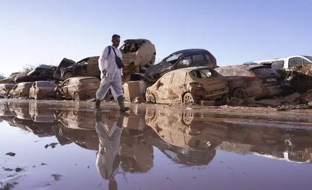 A man walks past stacked up cars after floods in Catarroja that left hundreds dead or missing in the Valencia region in Spain, Tuesday, Nov. 12, 2024. (AP Photo/Alberto Saiz)