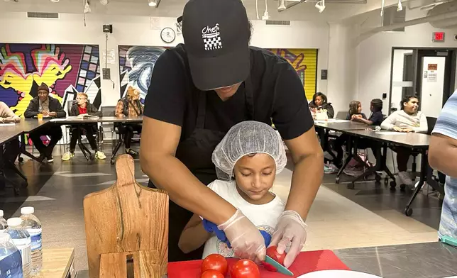 Chef Sharrie Agee helps Yareni Orduna-Herrera slice tomatoes for a margherita pizza as part of the Milwaukee Public Library Snack Hack, an after school nutrition program that teaches kids how to make healthy meals at home, Nov. 19, 2024, in Milwaukee. (AP Photo/Devi Shastri)