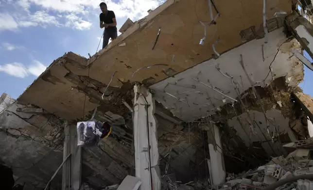 A man lowers a bag of his family's clothing from the roof of his destroyed house after he returned to his village of Hanouiyeh, southern Lebanon, Thursday, Nov. 28, 2024. (AP Photo/Hussein Malla)