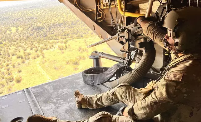 Osprey flight engineer Tech Sgt. Brett McGee sits on the back open ramp of the V-22 and holds the aircraft's .50 caliber gun as the crew flies over a New Mexico training range Oct. 9, 2024, near Cannon Air Force Base. (AP Photo/Tara Copp)